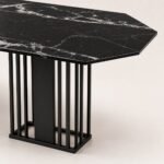 Detaliu generat al blatului negru venat, capătului teșit și bazei metalice lamelare