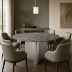 Masă de dining rotundă Triskel cu blat mineral gri-verde și soclu prismatic auriu, ambient de dining generat